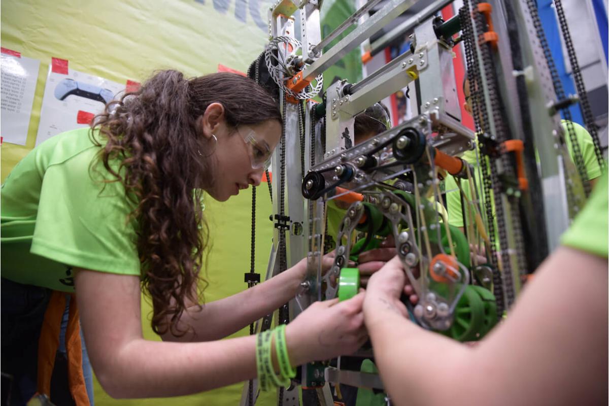 תמונה של תלמידת FIRST Robotics Competition עובדת על תיקון רכיבים מכאנים ברובוט.