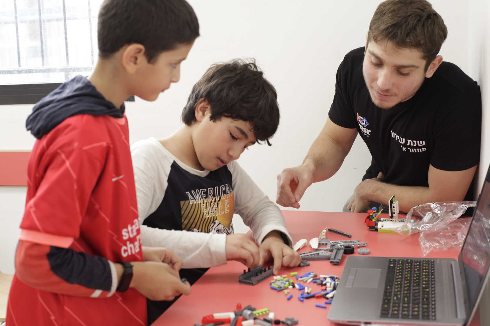 מתנדב שנת שירות מדריך 2 תלמידים צעירים הבונים ב-LEGO