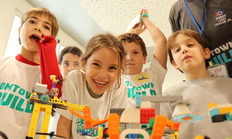 ילדה צעירה עם חבריה לקבוצה לצד דגמי ה-LEGO שבנו