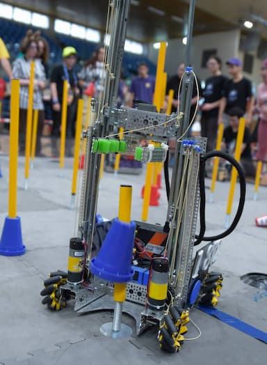 רובוט FIRST Tech Challenge העשוי מחלקי מתכת על מגרש, מניח קונוס משחק על עמוד